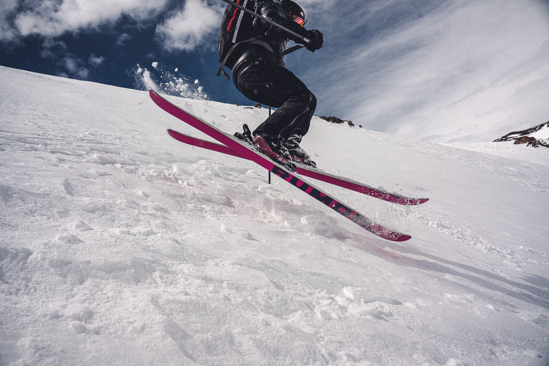 A skier popping off the snow on magenta skis, shot from low down