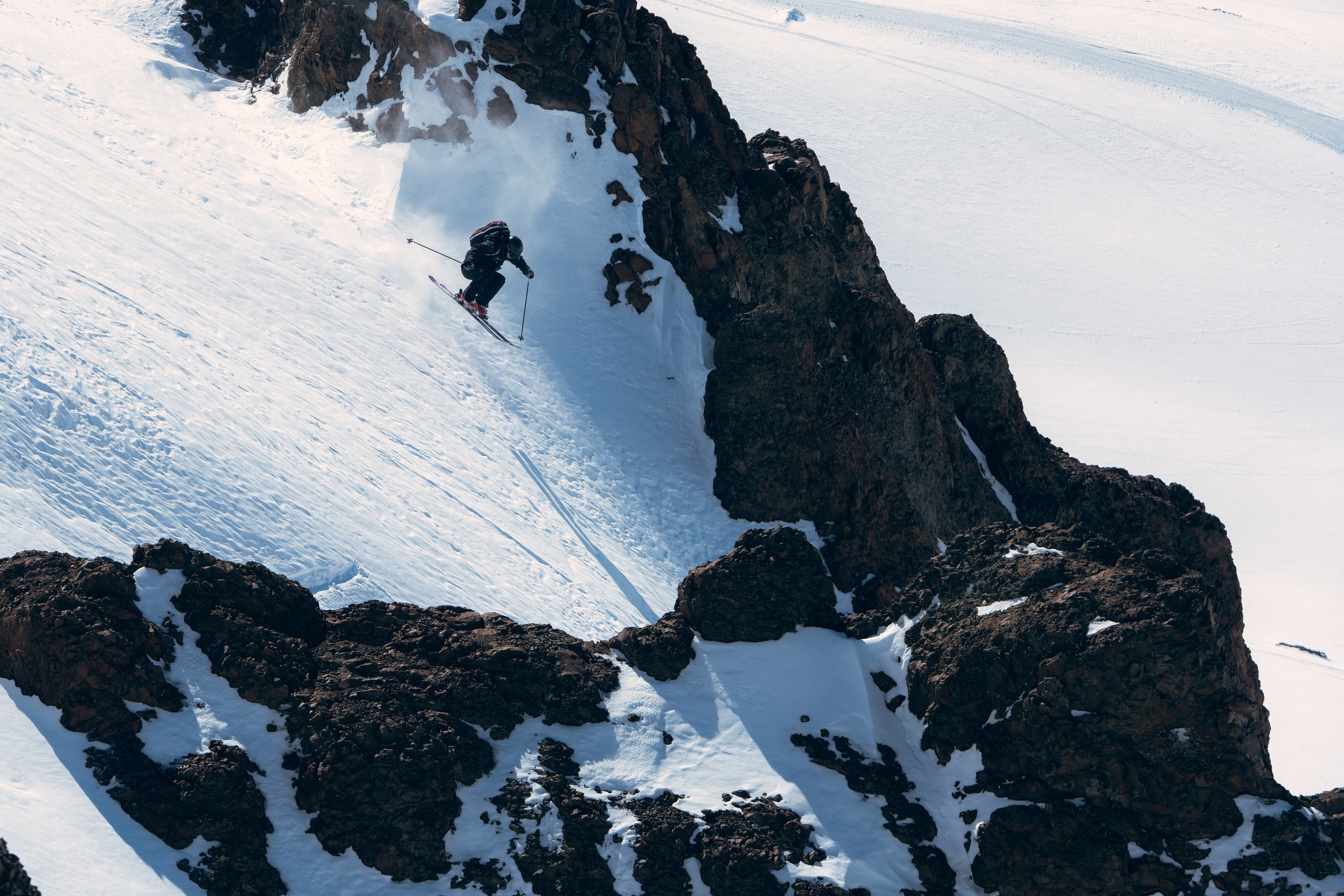 A skier dropping into a steep line beside a band of dark rock
