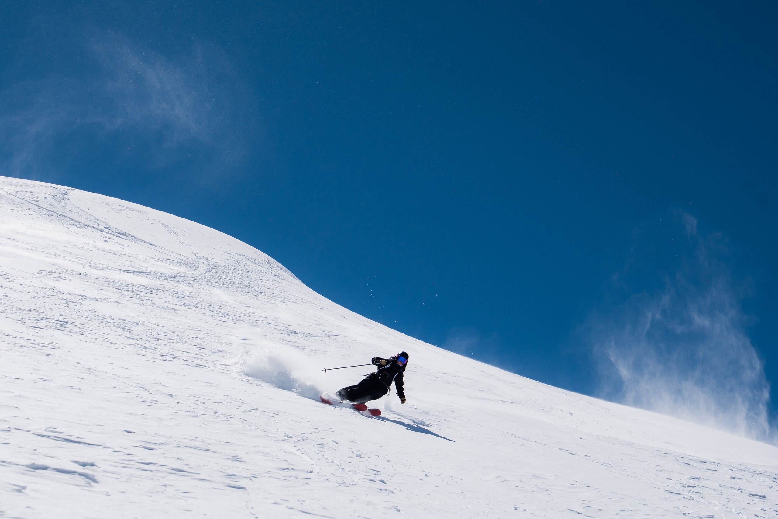 A skier carving a long turn across an open snowfield under a deep blue sky